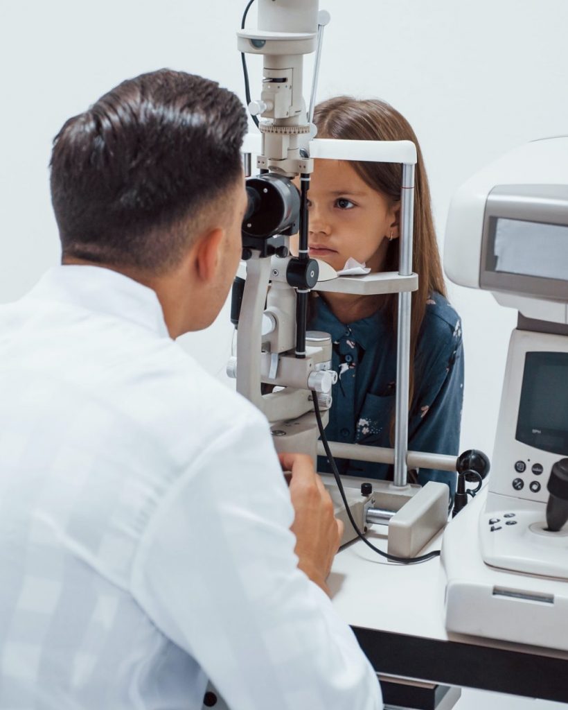 Young ophthalmologist is with little female visitor in the clinic